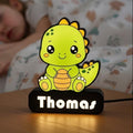 Veilleuse NextLab Studio personnalisée en forme de dinosaure vert sur une table de chevet près d'un enfant endormi.